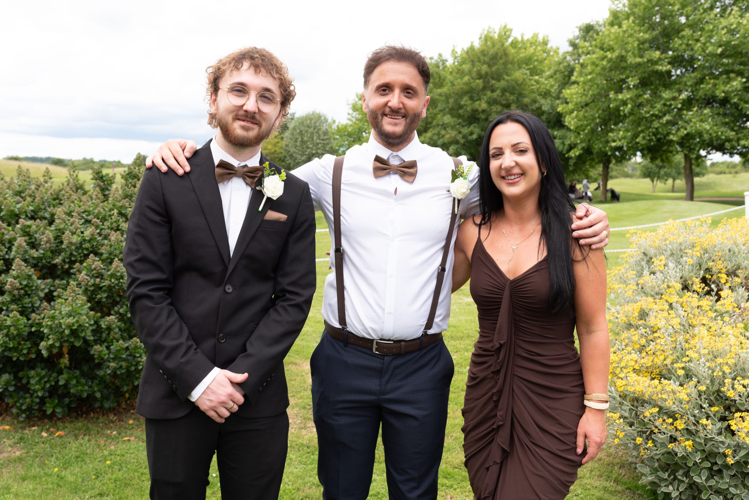 Two men in suits and a woman in a brown dress at an outdoor event.
