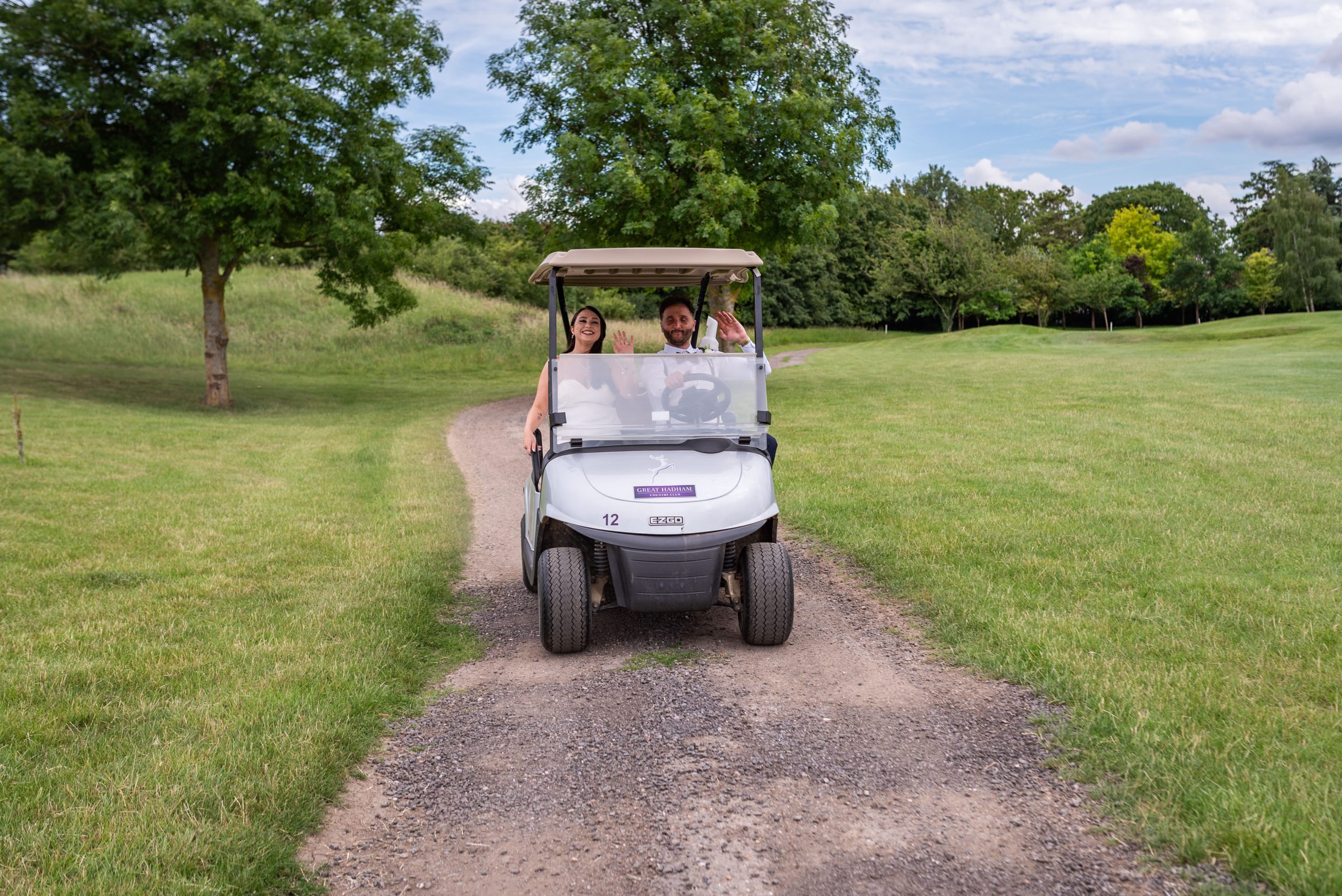 Couple in a golf cart on a scenic golf course, waving hello.