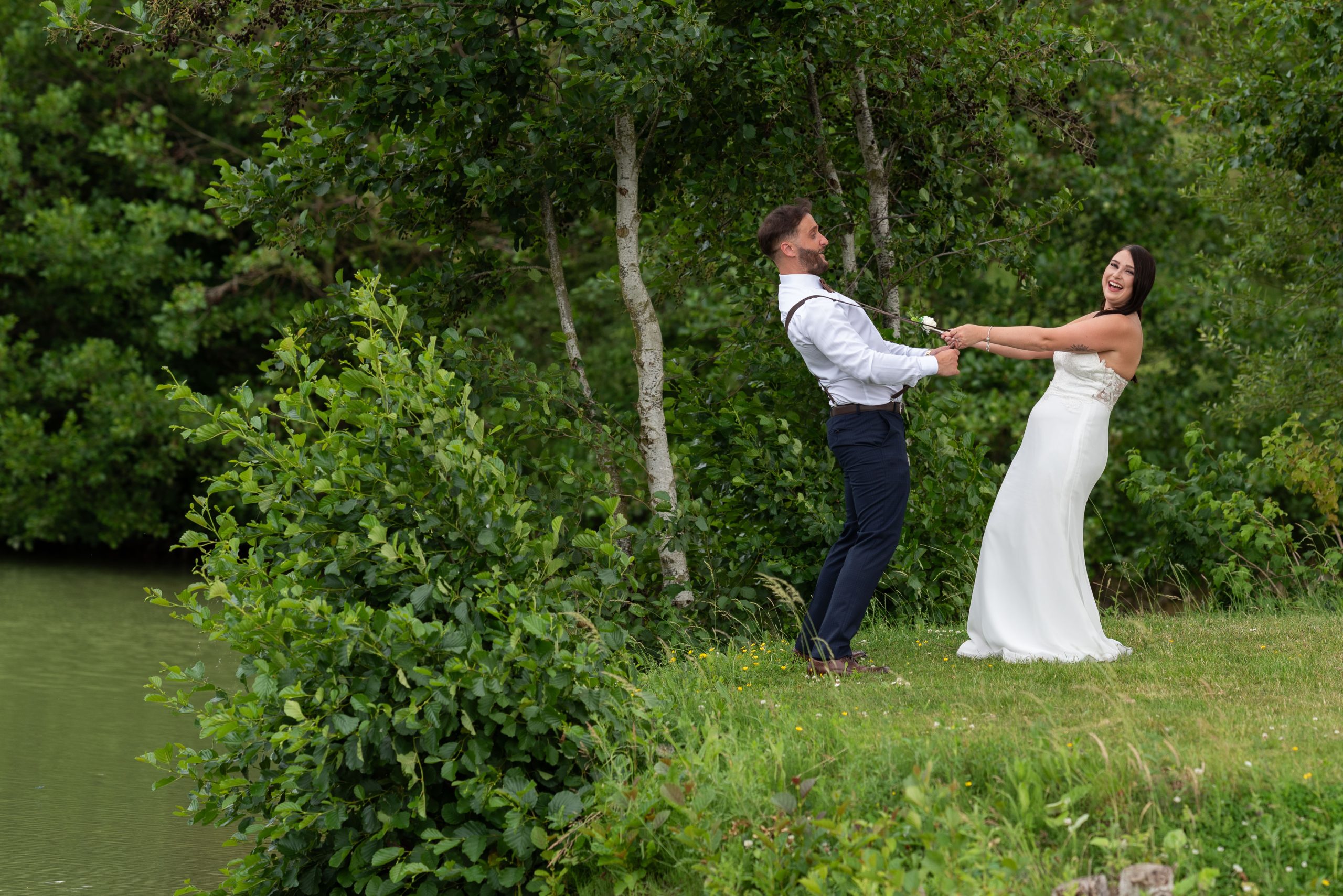 Newlyweds dancing by a lake, bride in white dress, groom in suit